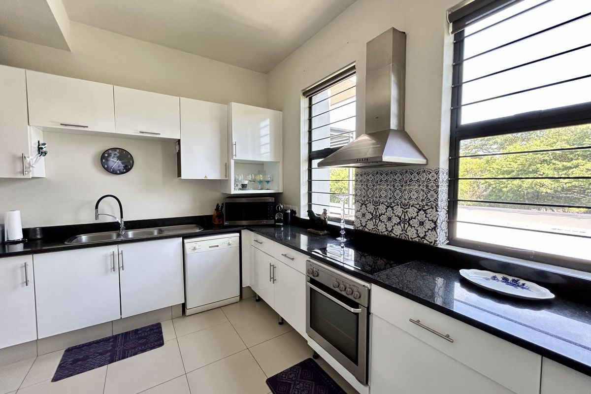 Modern kitchen featuring white cabinetry, black granite countertops, stainless steel appliances, and a decorative tiled backsplash with ample natural light.