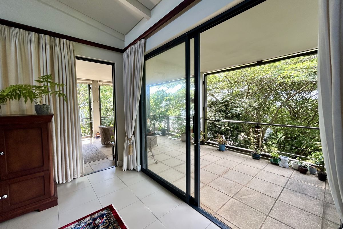 Bright living area featuring large sliding glass doors that open onto a spacious balcony with lush green views.