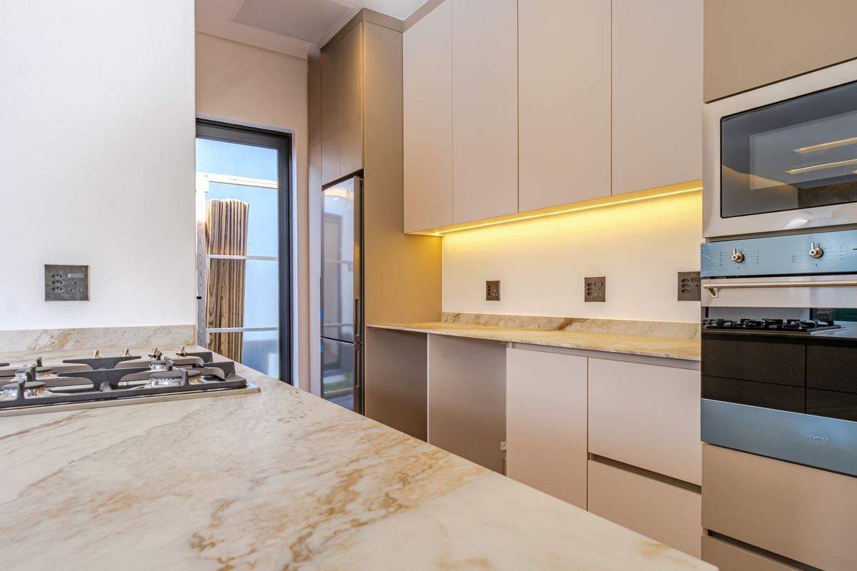 Modern kitchen featuring marble countertops, integrated cabinetry, built-in oven, gas cooktop, and under-cabinet lighting in a clean, contemporary design.