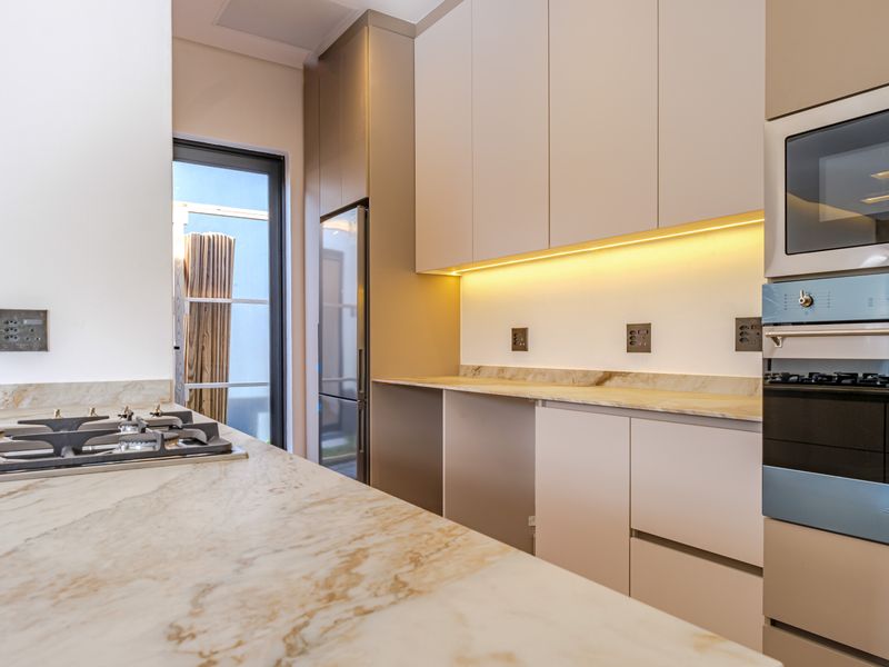 Modern kitchen featuring marble countertops, integrated cabinetry, built-in oven, gas cooktop, and under-cabinet lighting in a clean, contemporary design.