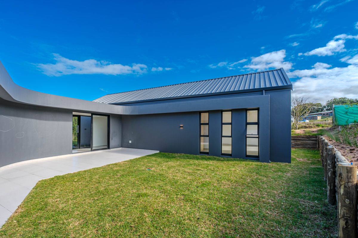 Modern rear exterior view featuring a dark grey facade, metal roof, tiled patio area, and landscaped lawn.