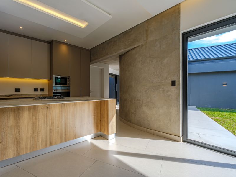 Modern kitchen featuring sleek cabinetry, integrated appliances, a stone island, and a striking curved concrete wall with direct access to the outdoor area.