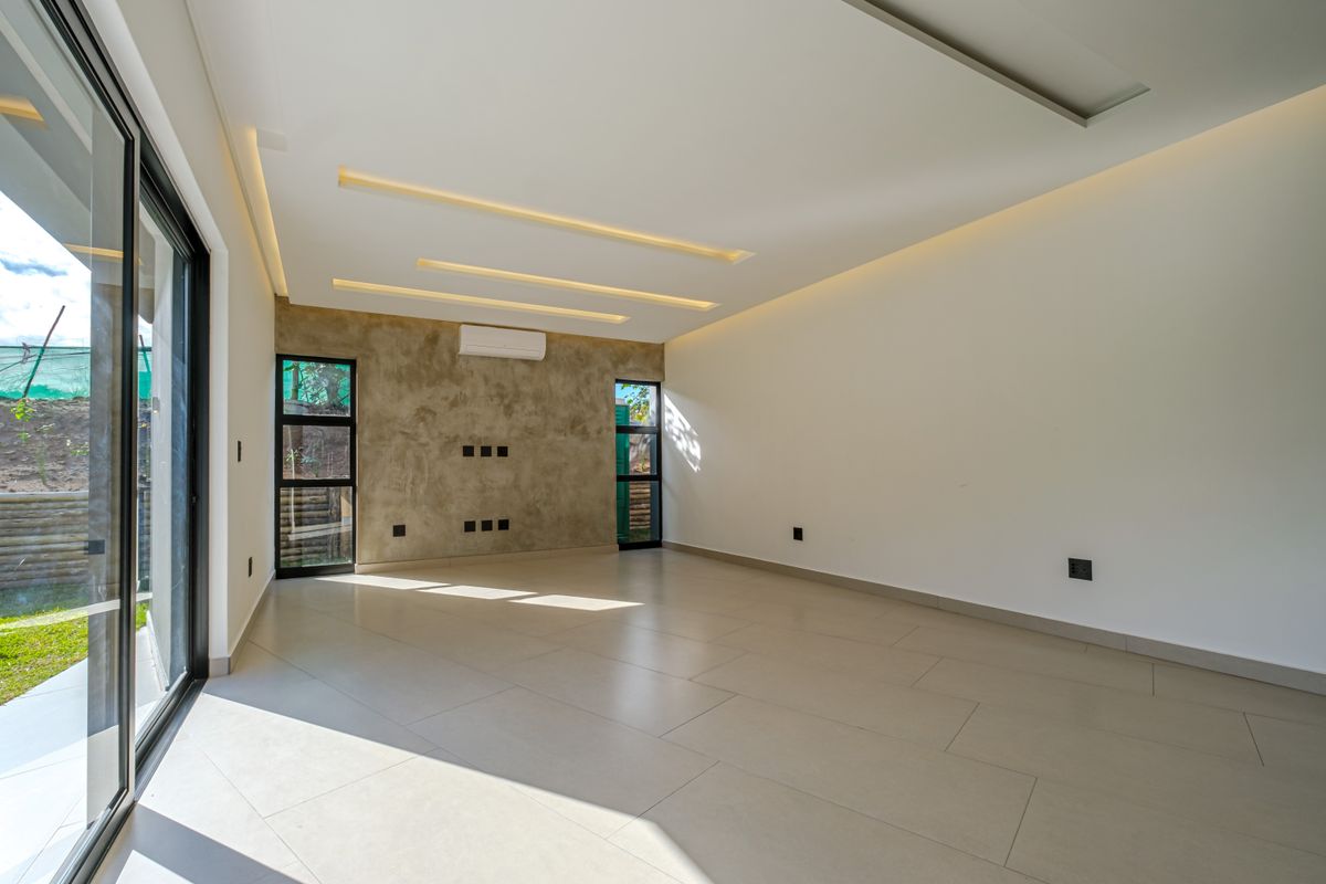 A bright, modern, and empty living room featuring large format floor tiles, a textured feature wall, recessed ceiling lighting, and sliding glass doors to the garden.