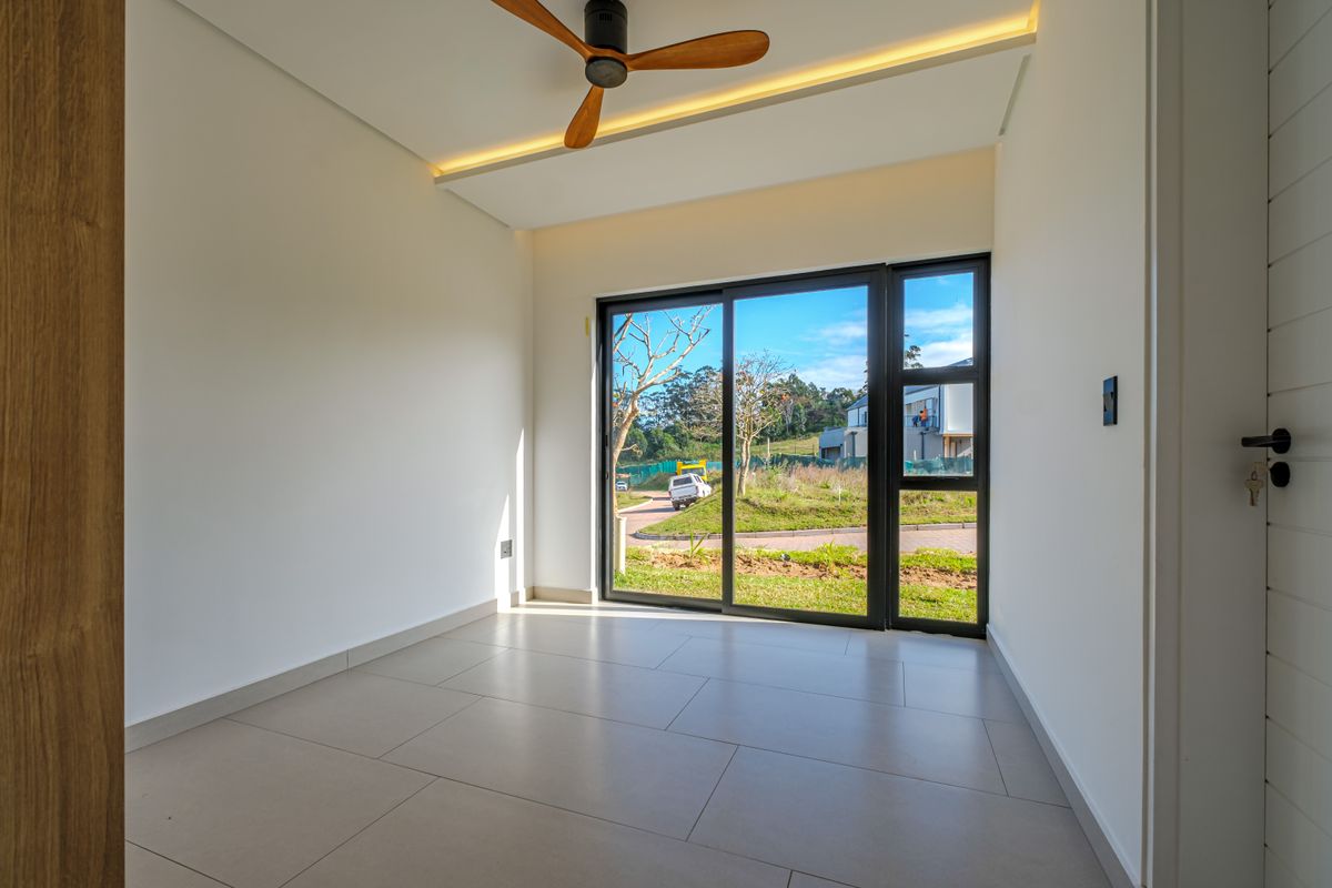 A bright, modern bedroom featuring tiled flooring, a ceiling fan, recessed lighting, and a large sliding glass door with views of the surrounding area.