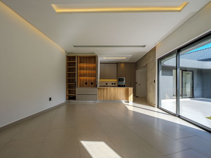 Modern open-plan living and kitchen area featuring sleek built-in cabinetry, recessed ceiling lighting, and large sliding glass doors leading to an outdoor space.