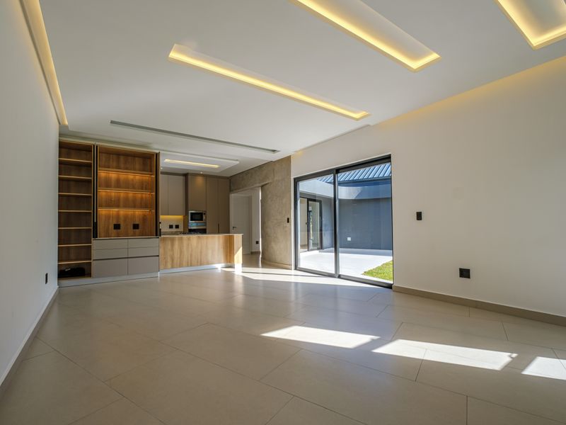 Modern open-plan living area featuring tiled floors, recessed ceiling lighting, and a sleek kitchen with built-in cabinetry, flowing seamlessly to an outdoor patio.