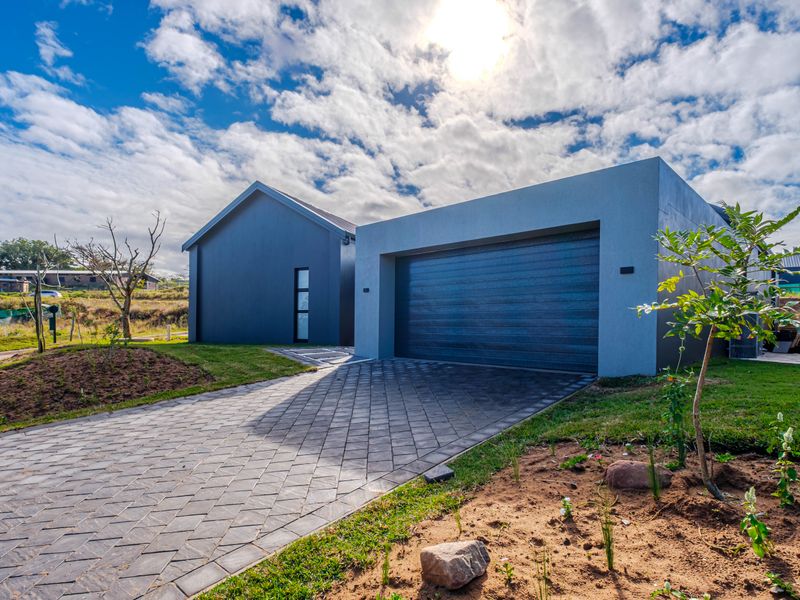 Modern front elevation featuring a paved driveway leading to a double garage with a contemporary dark grey facade.