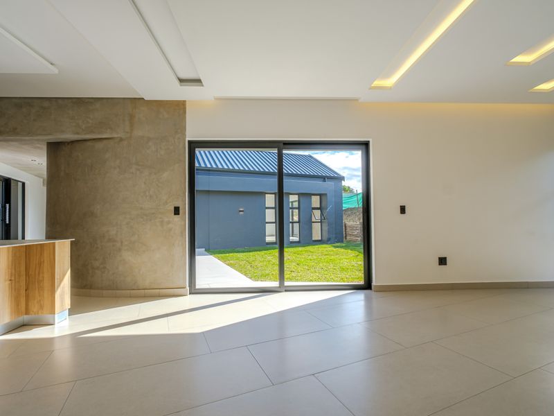 Modern open-plan living area featuring sleek tiled floors, recessed ceiling lighting, and large sliding glass doors opening to a private garden.