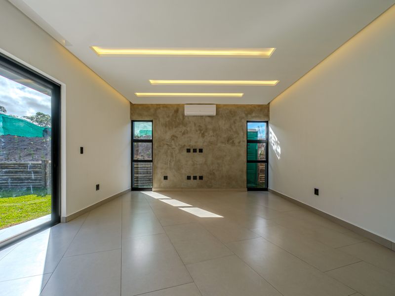 A bright, modern living area featuring large format floor tiles, recessed ceiling lighting, a textured feature wall, and direct access to the garden.