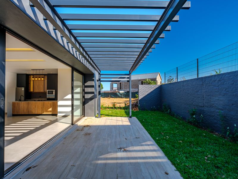 Modern covered patio featuring a sleek pergola, tiled flooring, and seamless indoor-outdoor flow through large sliding glass doors to the garden.