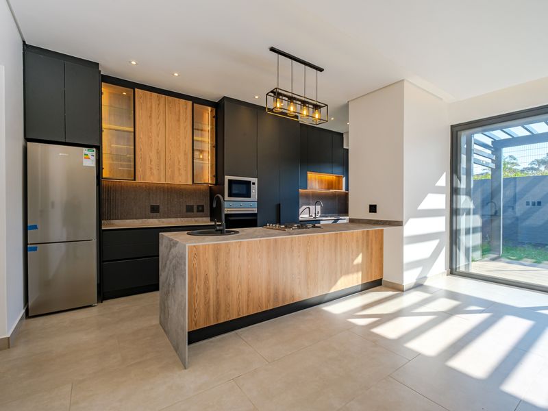 Modern kitchen featuring a central island, sleek dark cabinetry with wood accents, built-in appliances, and direct access to an outdoor patio area.