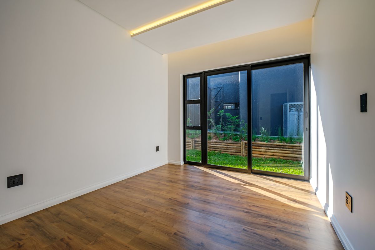 A bright, modern, empty bedroom featuring laminate flooring, recessed ceiling lighting, and a large sliding glass door providing access to the garden.