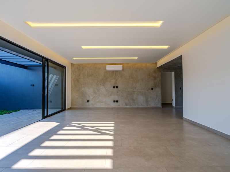 Spacious, modern living area featuring recessed ceiling lighting, a textured feature wall, split-system air conditioning, and large sliding doors opening to an outdoor patio.