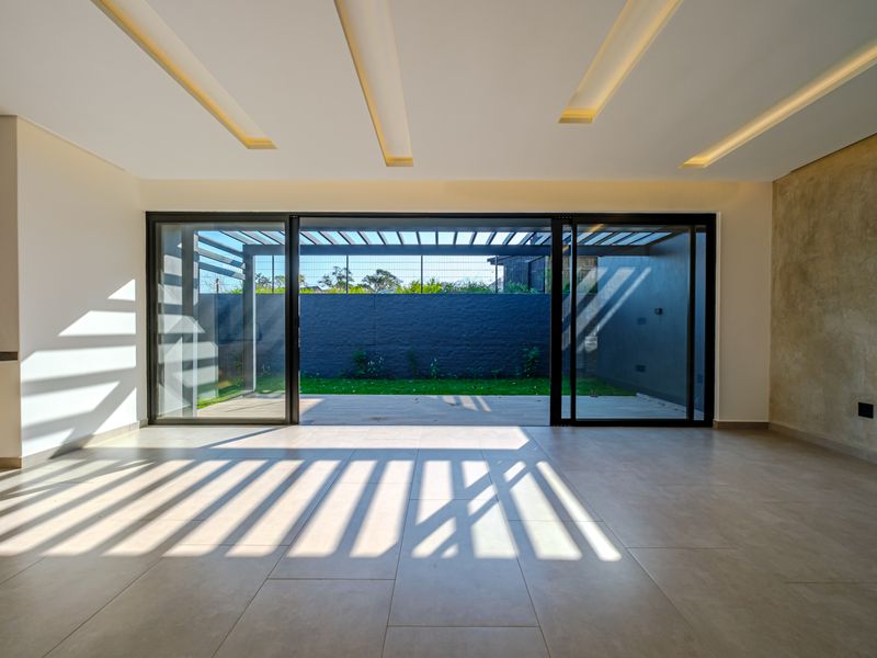 Spacious open-plan living area featuring modern recessed ceiling lighting, large sliding glass doors, and seamless access to a private rear garden with a pergola.
