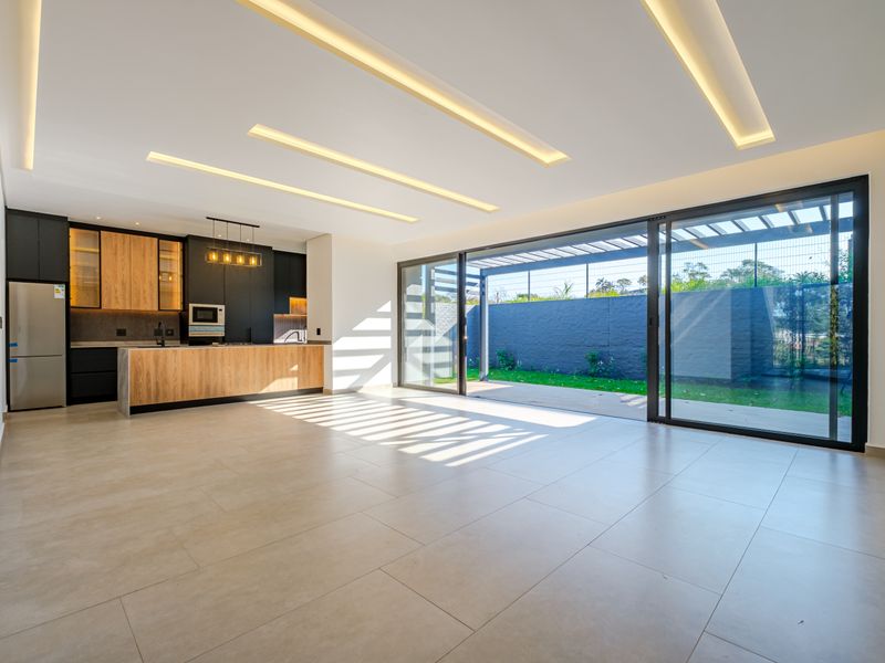 Modern open-plan living area featuring a sleek kitchen with wood-accented cabinetry, recessed ceiling lights, and large sliding doors opening to a private rear garden.