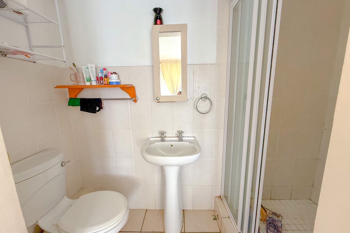 A functional bathroom featuring a pedestal sink, a standard toilet, and a glass-enclosed shower stall with tiled walls.