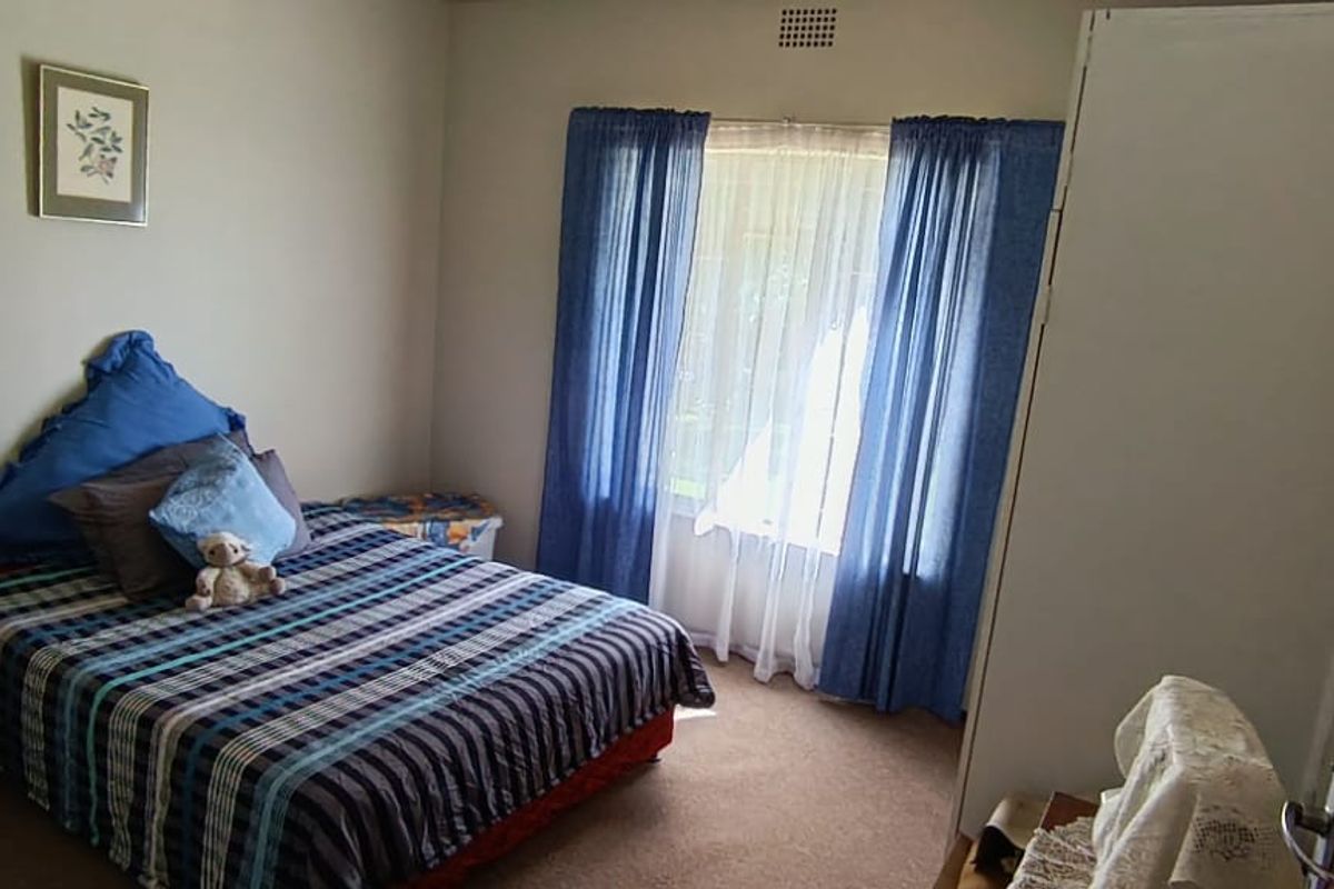 A standard bedroom featuring carpeted flooring, a built-in cupboard, and a window with curtain tracks.