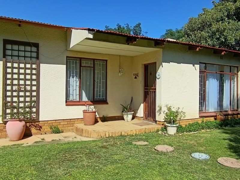 Front elevation of a single-story house featuring a covered entrance porch, brick base, and established garden area.