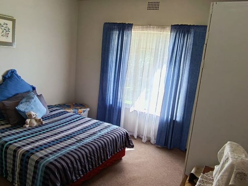 A standard bedroom featuring carpeted flooring, a built-in cupboard, and a window with curtain tracks.
