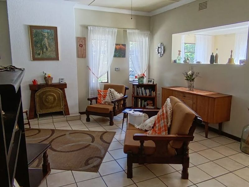 A living room featuring tiled flooring, a built-in fireplace, and a large wall cutout providing an open view into the adjacent room.