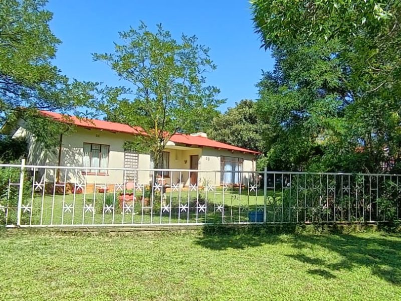 A single-story residential house featuring a red metal roof, set behind a white metal security fence with a spacious front lawn.