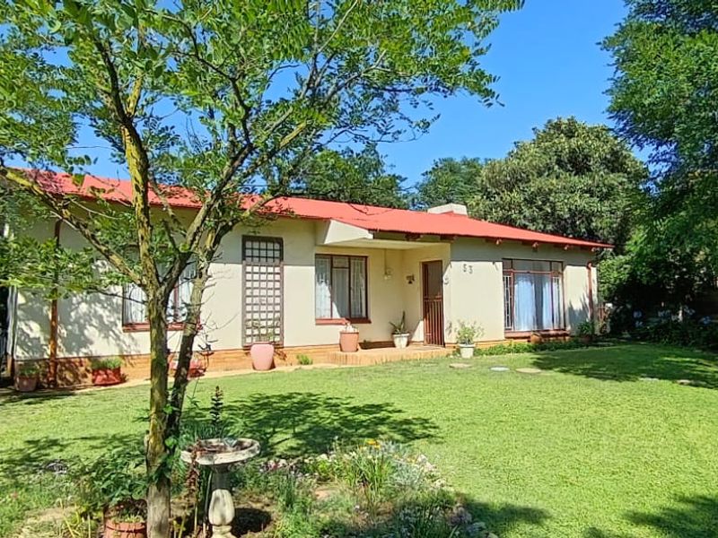 A charming single-story residential home featuring a red metal roof, established garden, and a welcoming front entrance area.