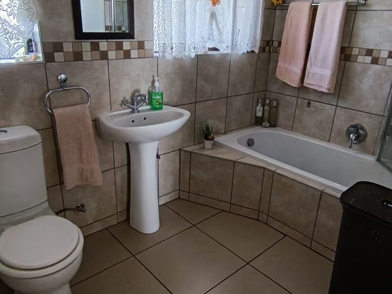 A functional bathroom featuring a pedestal basin, a built-in bathtub with a shower screen, and a standard toilet, finished with neutral wall and floor tiles.