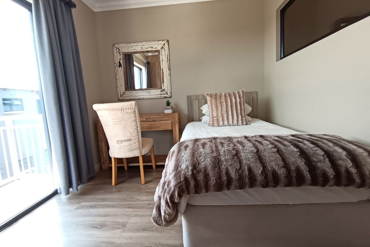 A well-maintained bedroom featuring modern laminate flooring, neutral wall tones, and a sliding glass door providing access to a private balcony.