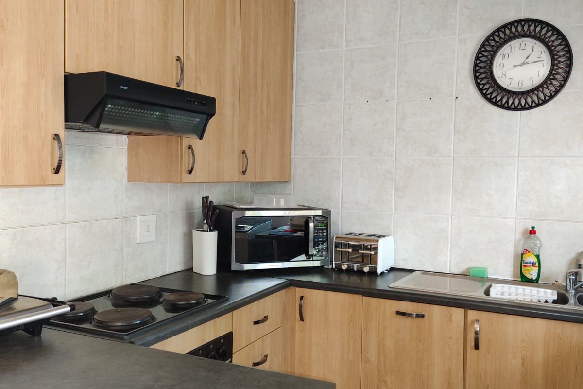 Functional kitchen featuring light wood-look cabinetry, dark laminate countertops, integrated electric hob, extractor fan, and tiled backsplash.