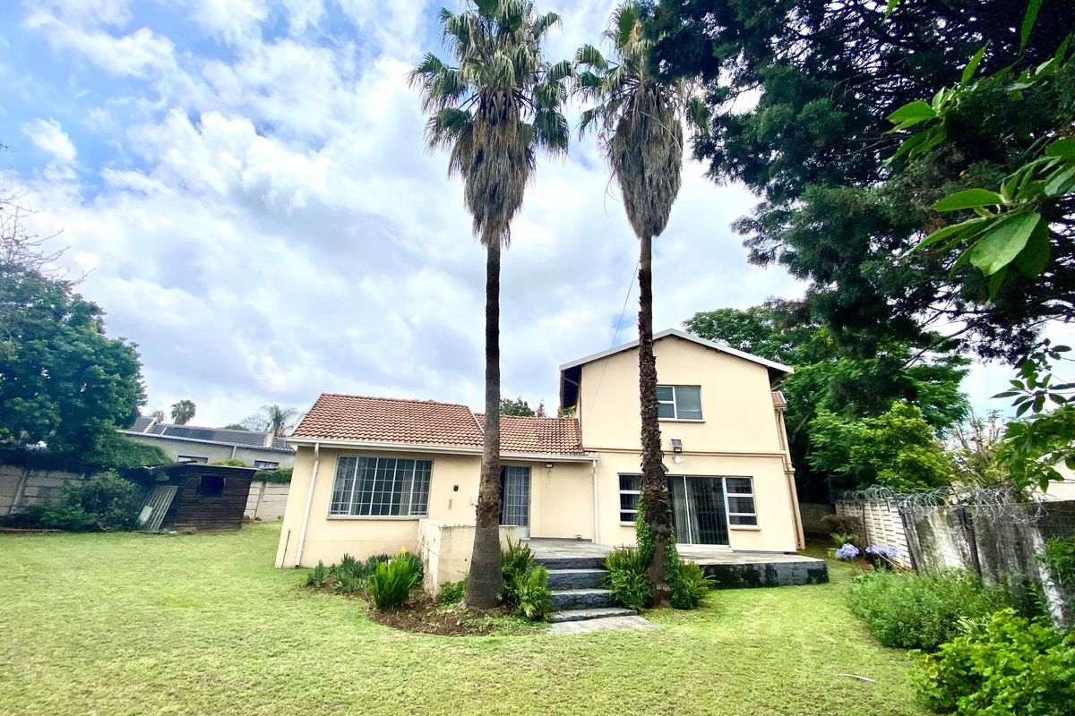 Rear view of a two-story house featuring a tiled roof, sliding glass doors, a concrete patio, and a spacious garden with mature palm trees.