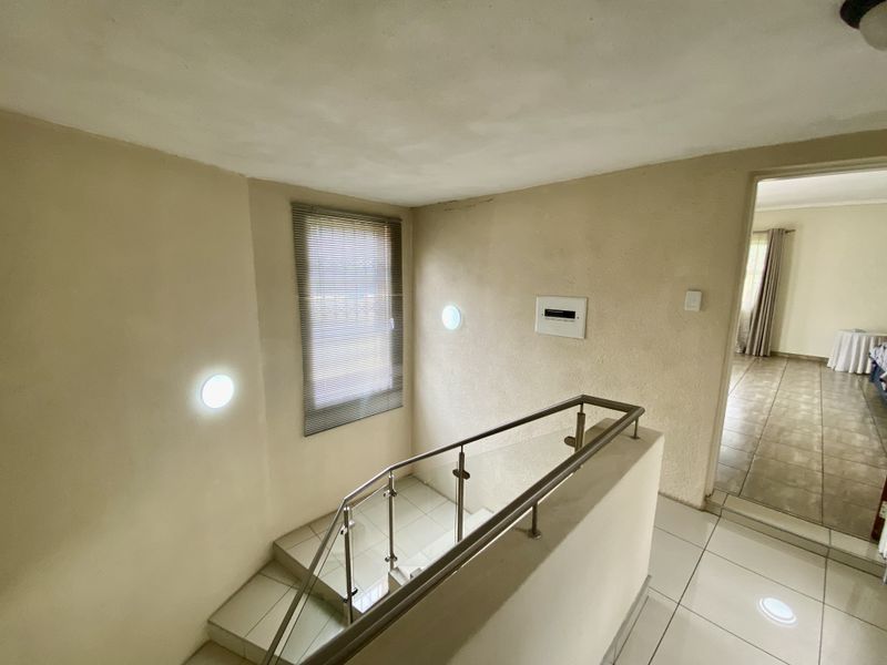 A bright hallway featuring a staircase with a modern stainless steel and glass balustrade, tiled flooring, and recessed wall lighting.