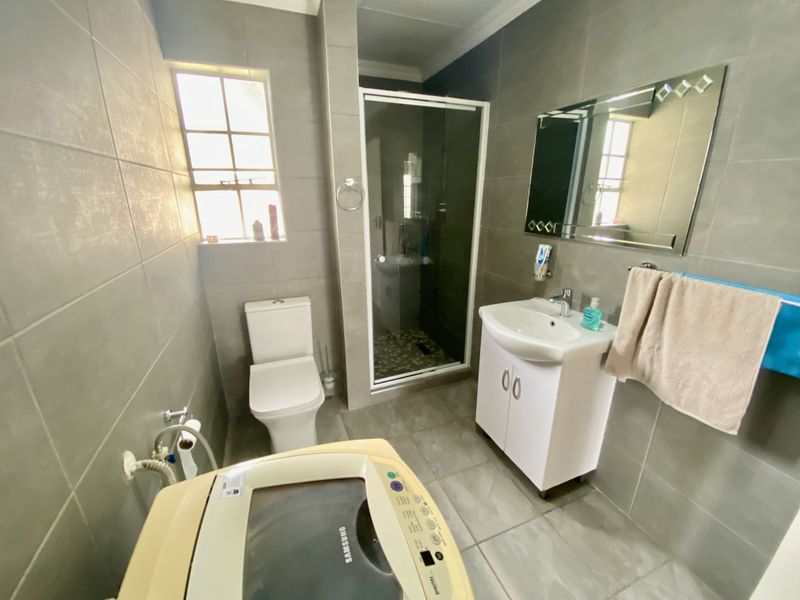 A functional bathroom featuring a shower enclosure, toilet, and vanity basin with modern grey wall and floor tiling.