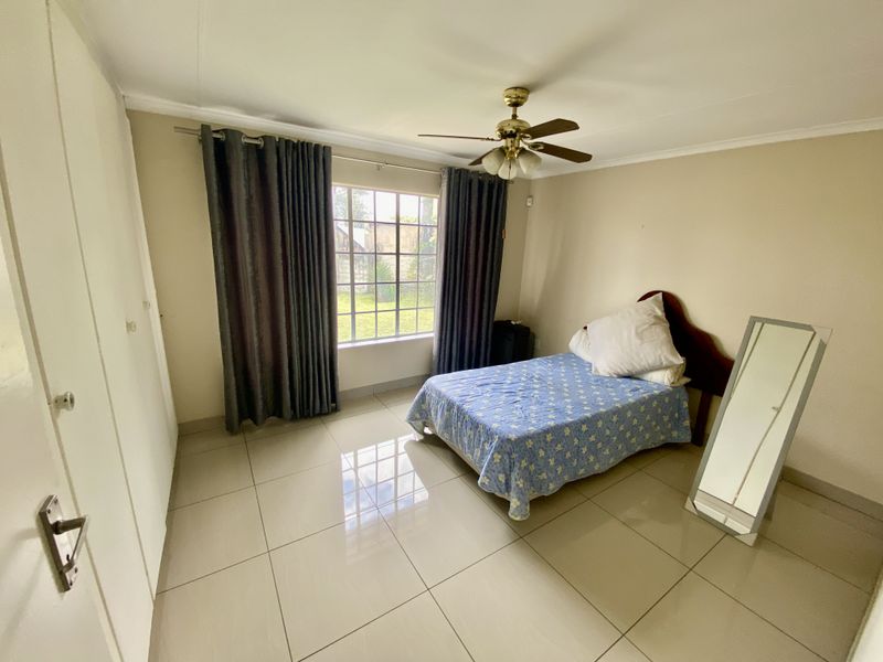 A well-lit bedroom featuring neutral tiled flooring, built-in cupboards, and a ceiling fan, offering a clean and functional living space.