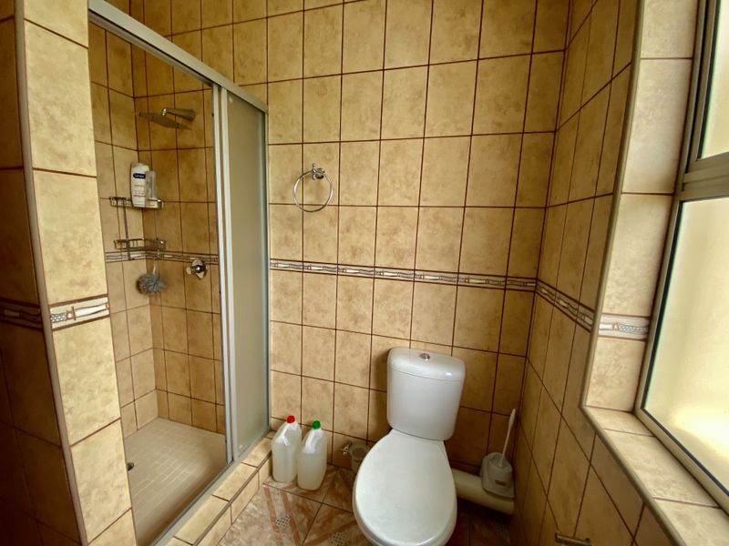 A functional bathroom featuring a shower enclosure, toilet, and full-height wall tiling with a decorative border.