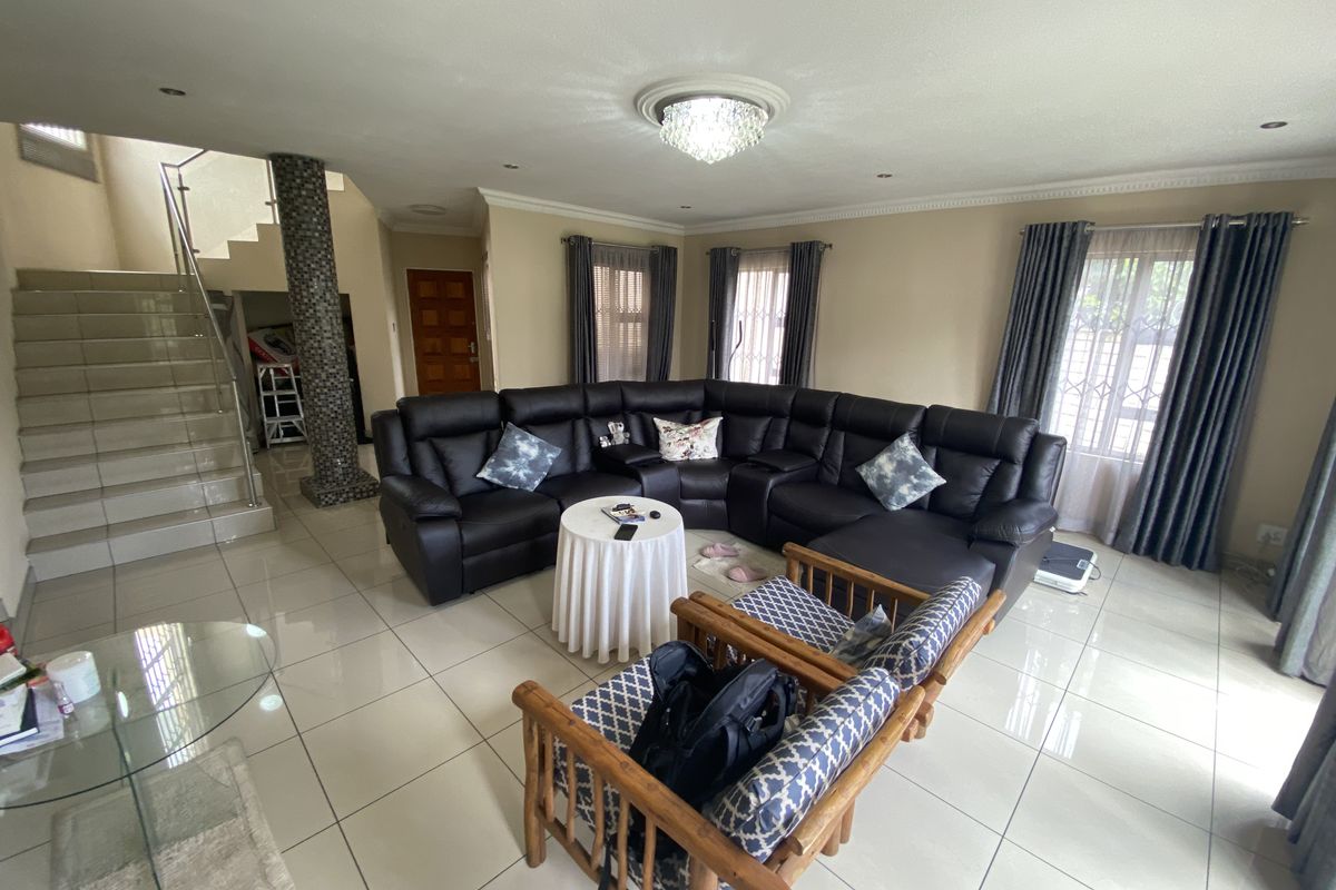 Spacious living room featuring large format floor tiles, a decorative mosaic pillar, and an open staircase with a modern glass balustrade.