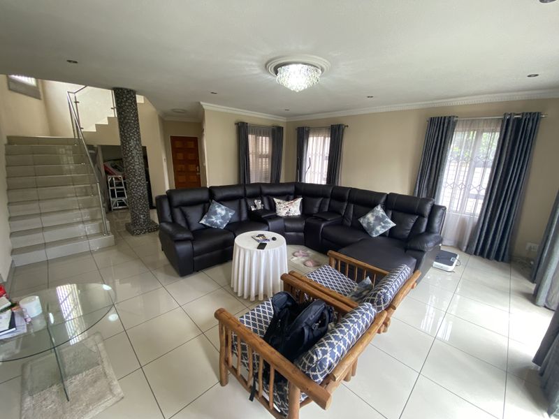 Spacious living room featuring large format floor tiles, a decorative mosaic pillar, and an open staircase with a modern glass balustrade.