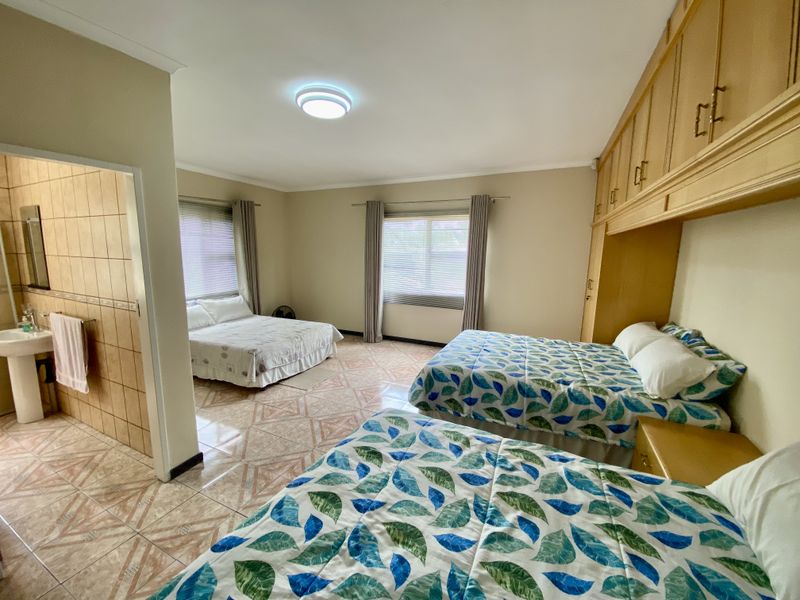 Spacious bedroom featuring built-in wooden cupboards, tiled flooring, and an attached en-suite bathroom with a pedestal basin.