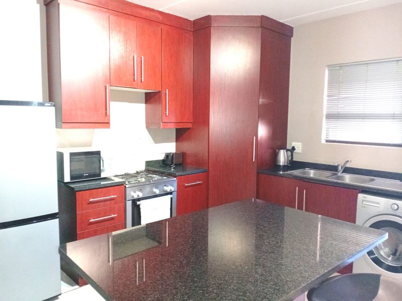 Functional kitchen featuring dark wood cabinetry, granite countertops, a gas hob, oven, and integrated space for laundry appliances.