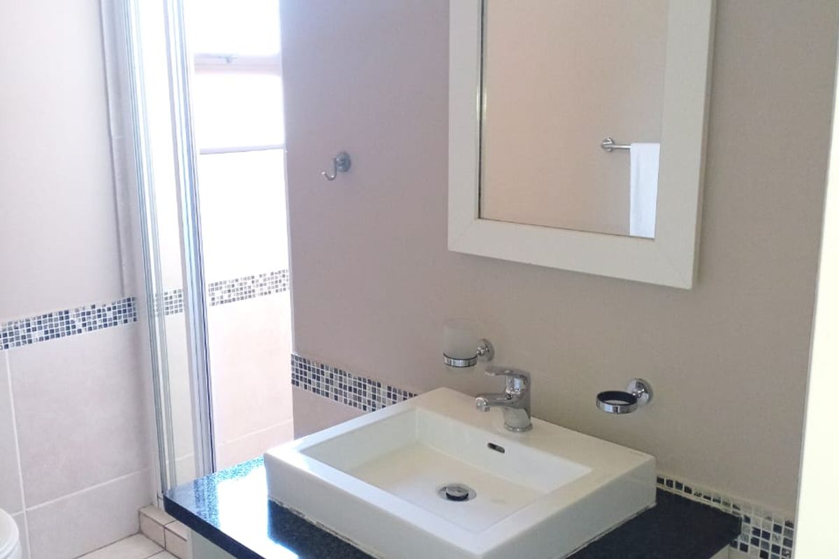 A clean bathroom featuring a modern vanity with a granite countertop, vessel sink, wall mirror, and a separate shower enclosure with tiled finishes.