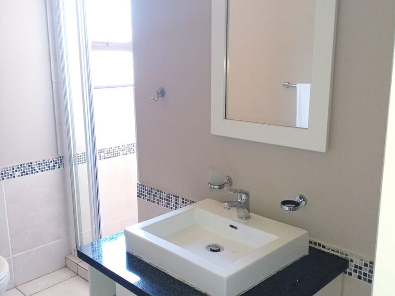 A clean bathroom featuring a modern vanity with a granite countertop, vessel sink, wall mirror, and a separate shower enclosure with tiled finishes.