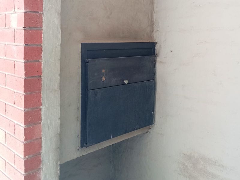 A close-up view of an exterior entrance area featuring a built-in metal mailbox set into a brick and plastered wall with tiled flooring.