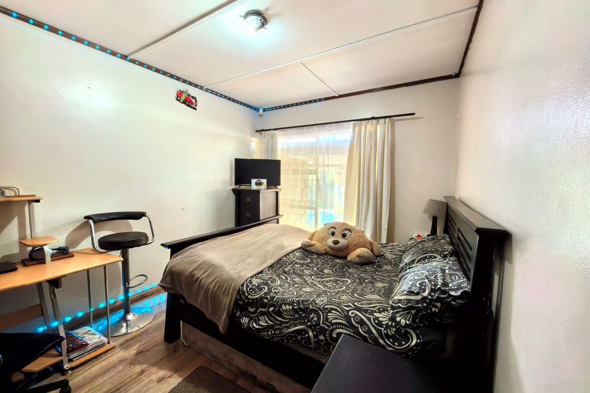 A functional bedroom featuring wood-look flooring, a large window with curtains, and integrated LED strip lighting along the ceiling perimeter.