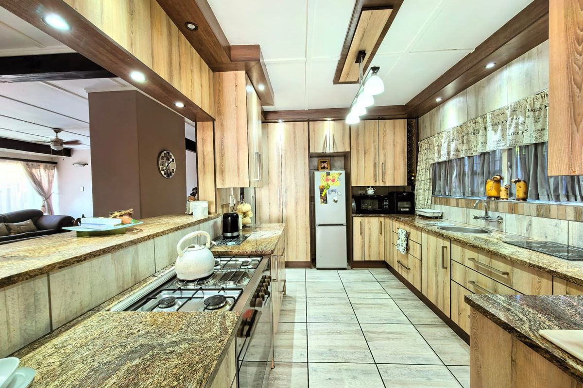 Spacious kitchen featuring wood-look cabinetry, granite countertops, a built-in gas hob, and integrated lighting, offering a functional and warm culinary space.