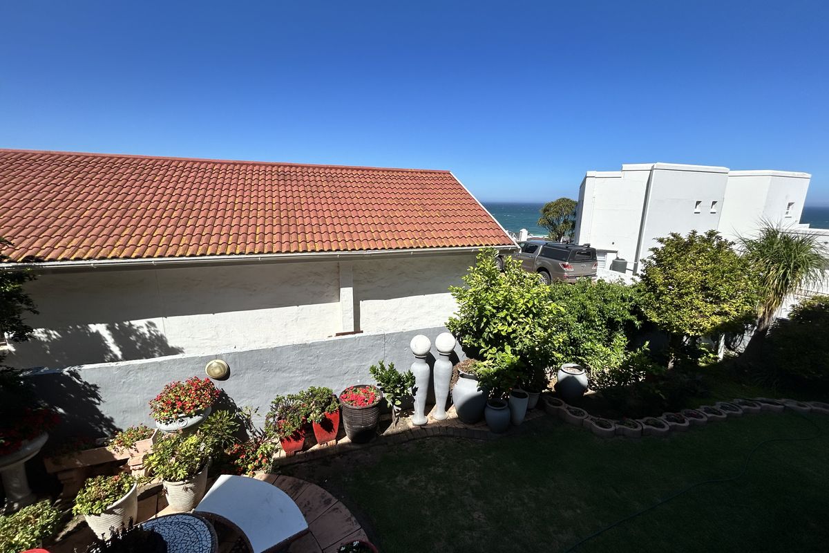 A well-maintained rear garden area featuring a lawn, landscaped borders, and a view of the ocean in the distance.