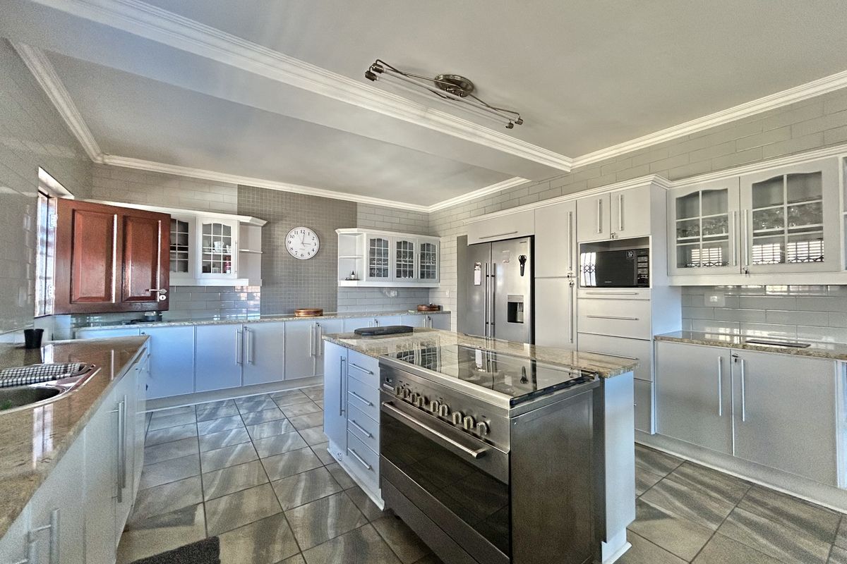 Spacious kitchen featuring a central island with a built-in stove, granite countertops, light-toned cabinetry, and tiled flooring throughout.