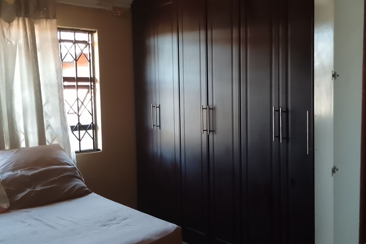 A bedroom featuring dark wood built-in wardrobes and security bars on the windows, providing functional storage and natural light.