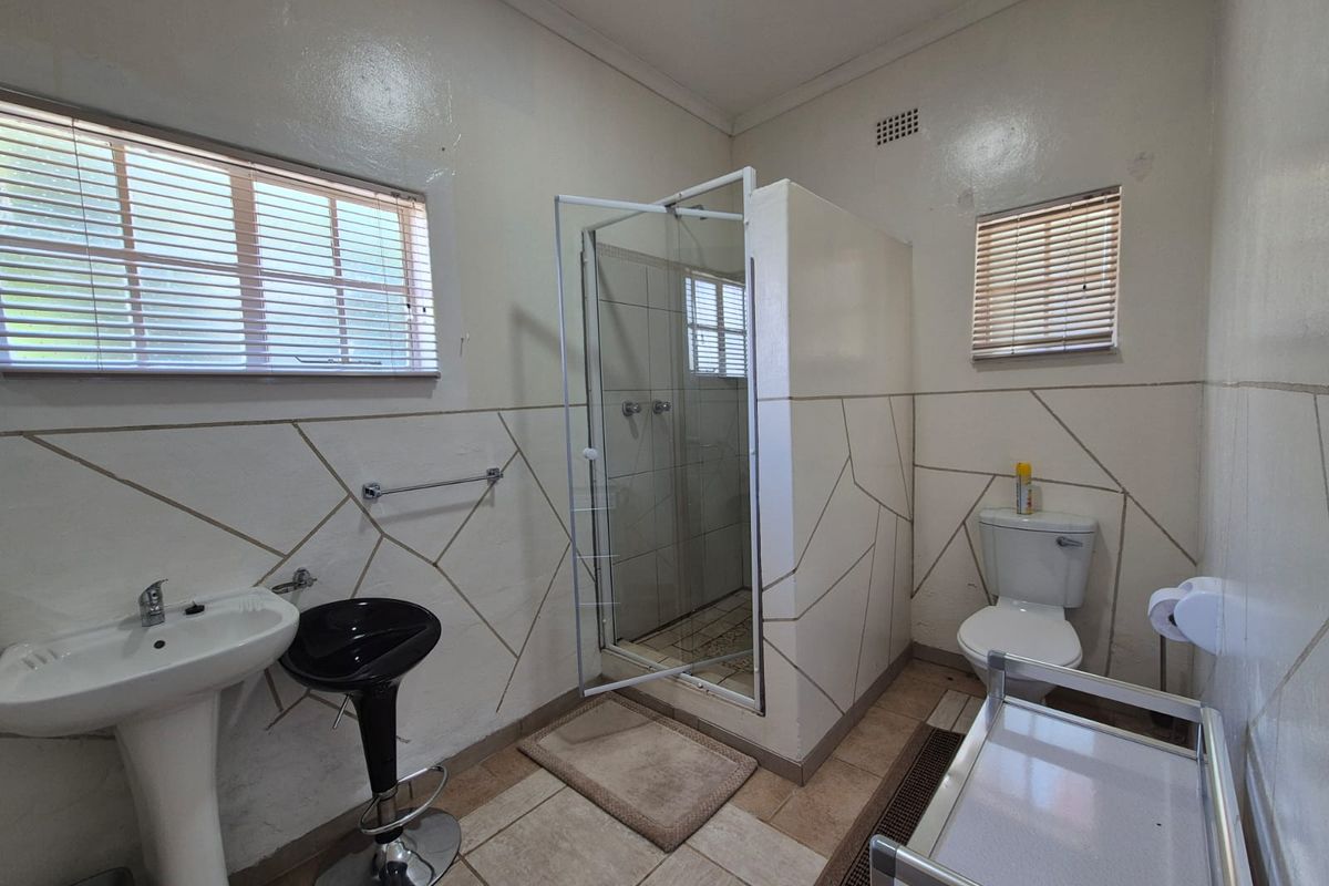 A functional bathroom featuring a pedestal basin, a glass-enclosed shower, and a standard toilet with tiled walls and flooring.