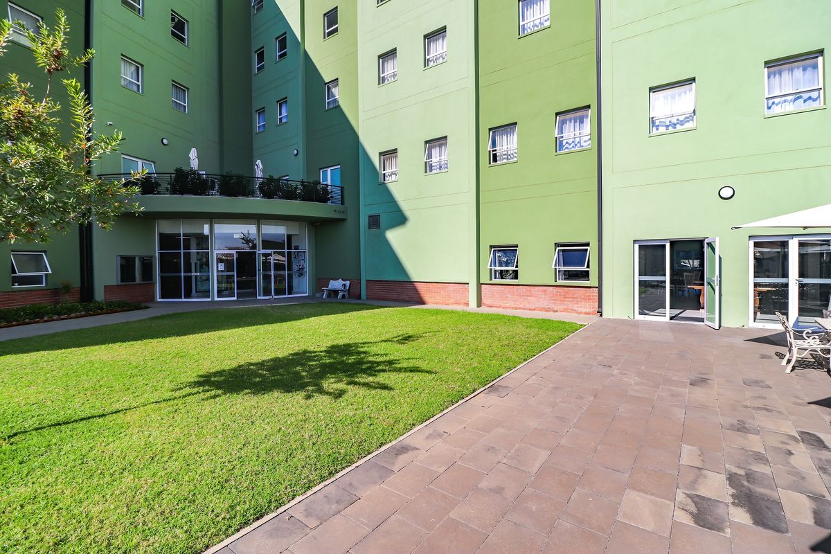 A view of the rear exterior courtyard featuring a paved patio area, a well-maintained lawn, and access to the building's ground floor.