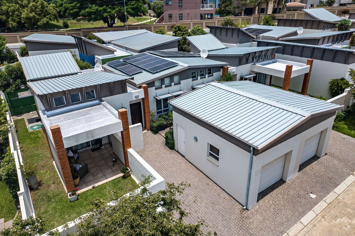 Aerial view of a modern townhouse complex featuring metal roofing, solar panels, paved driveways, and private patio areas.