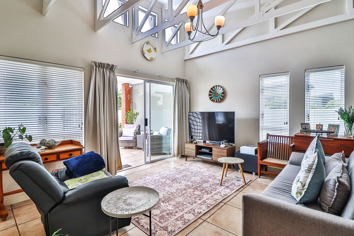 Spacious living room featuring high vaulted ceilings with exposed trusses, tiled flooring, and large sliding glass doors leading to an outdoor patio area.